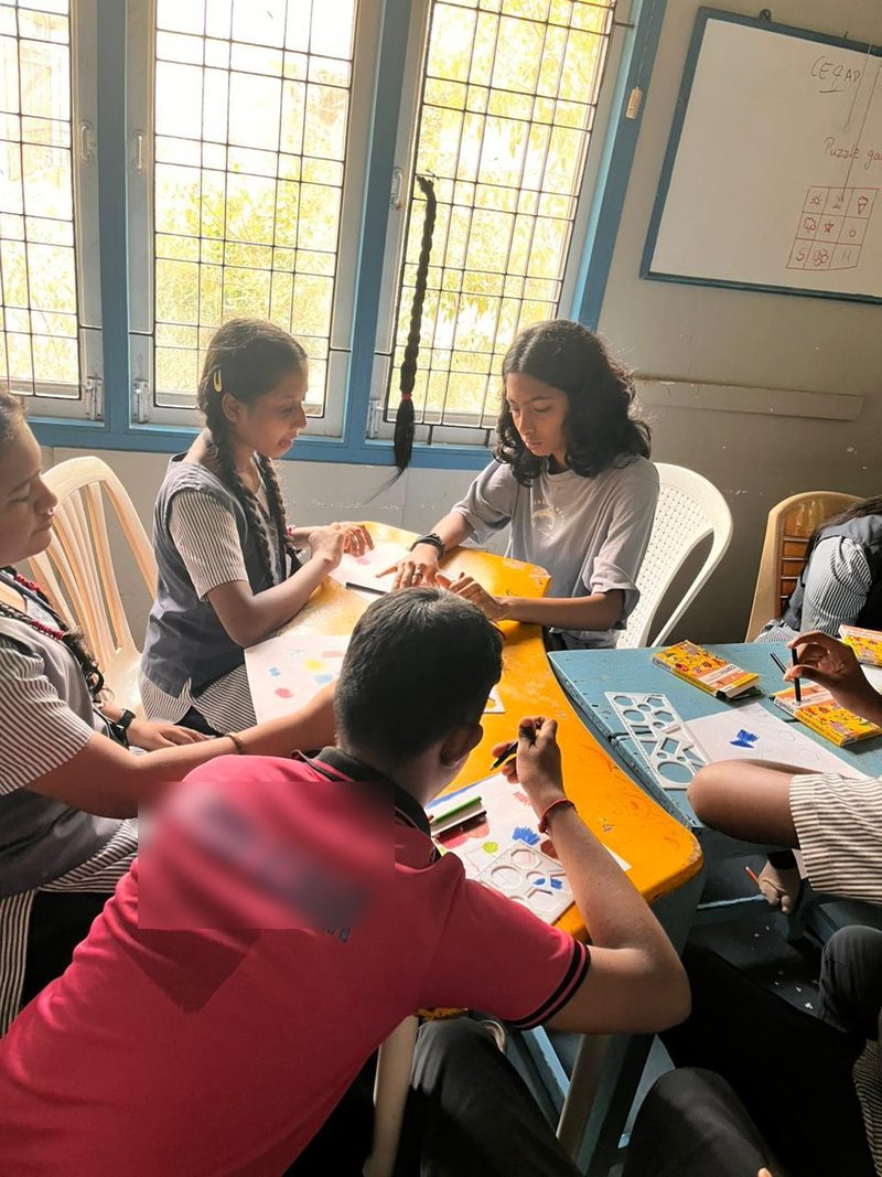 Shruti Arvind helping a student with a stencil drawing at a shared table